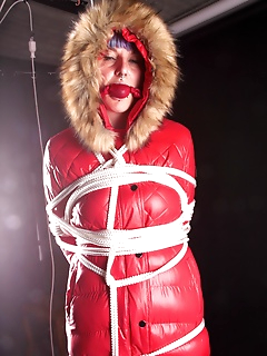 16 of Mara wearing a sexy black shiny nylon down pants and a brandnew red special down jacket tied and gagged overhead with ropes